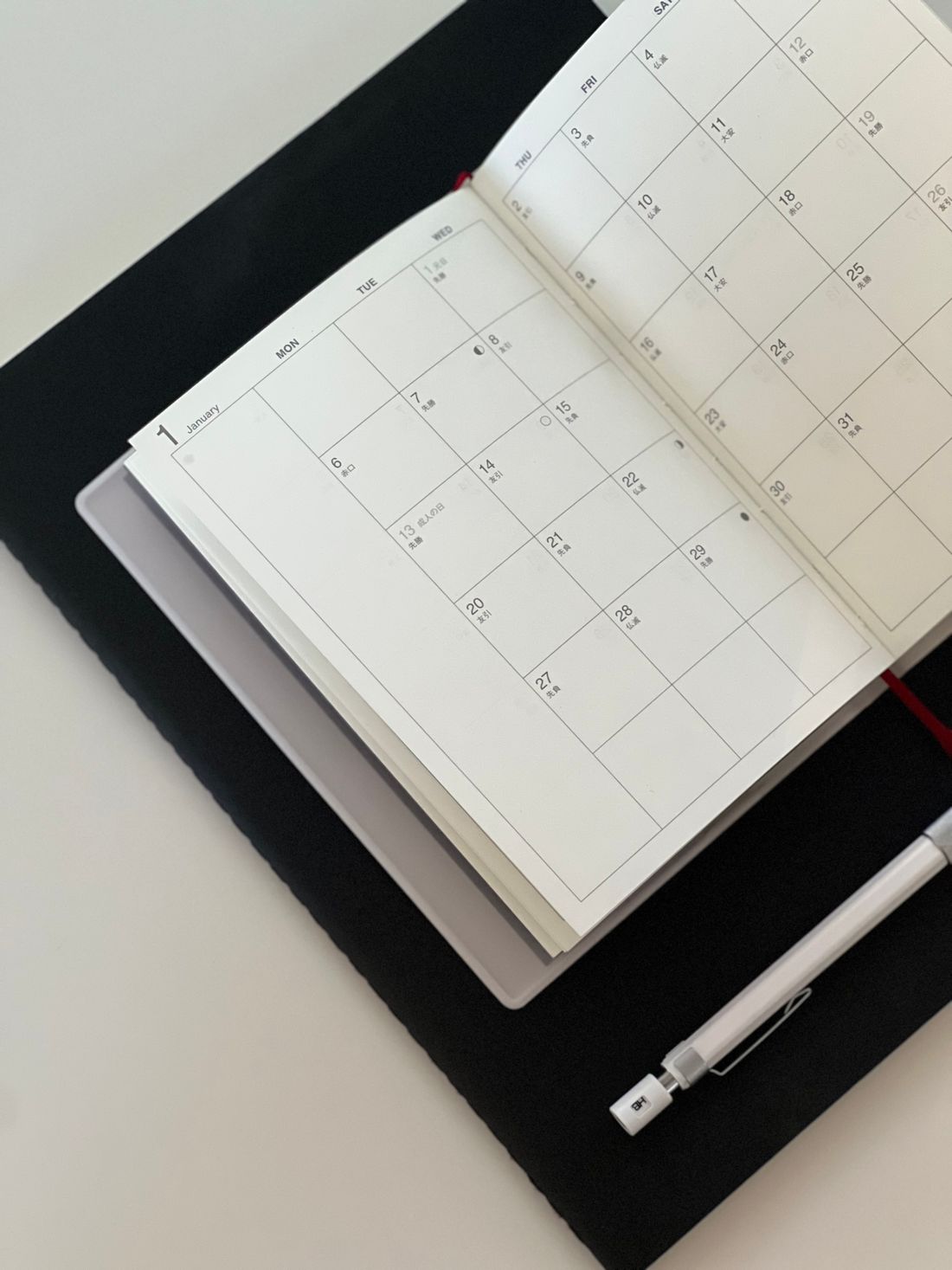 An open calendar planner beside a pen and tablet.