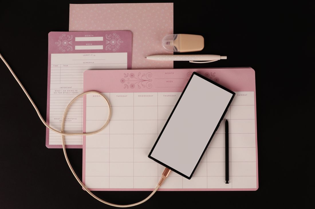 Planner, tablet and stationery on a dark desk.