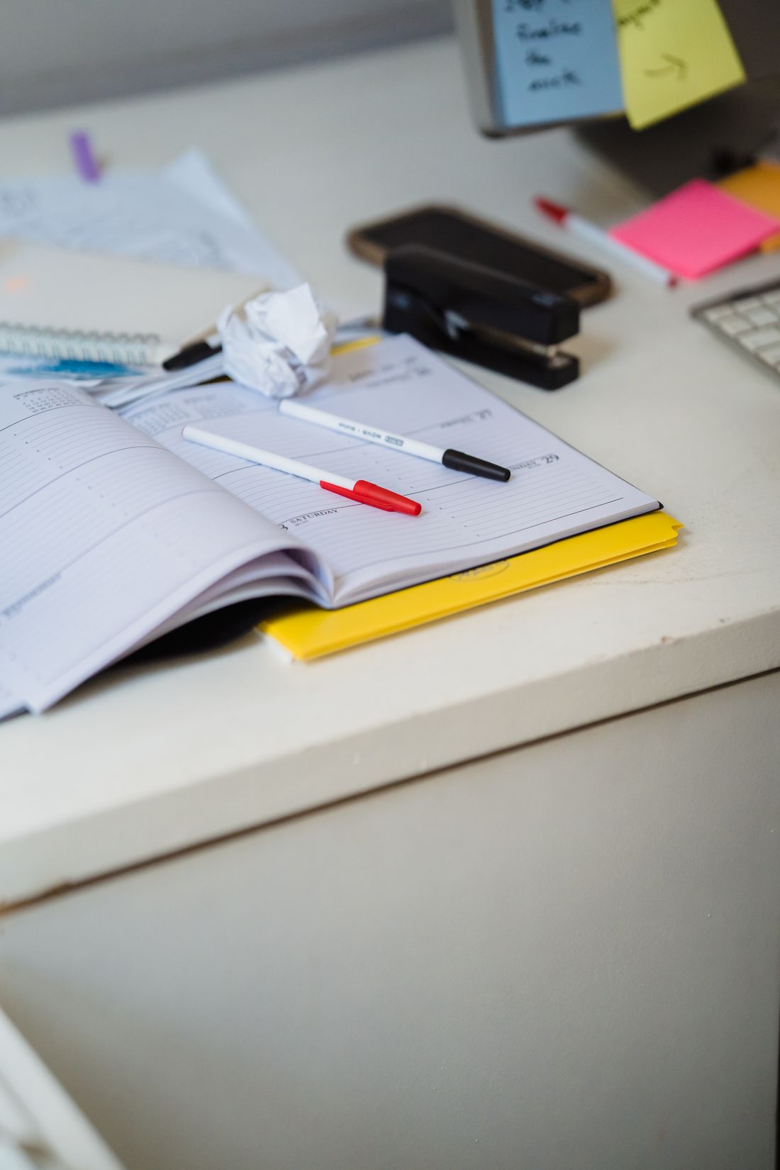 A planner, pens and office supplies on a desk.